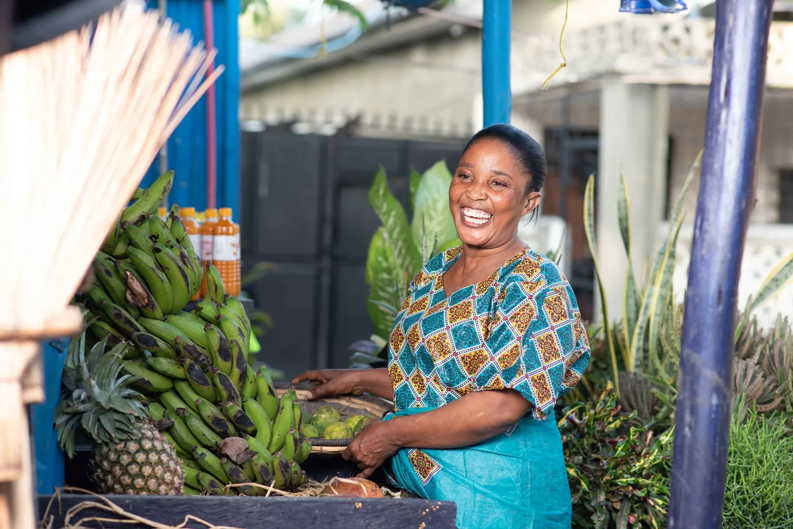 A laughing woman at a fruit stall of green bananas and pineapples in Dar es Salaam