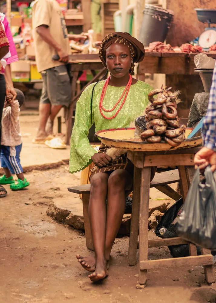A young woman in green and coral beads seated at a market table of dried fish
