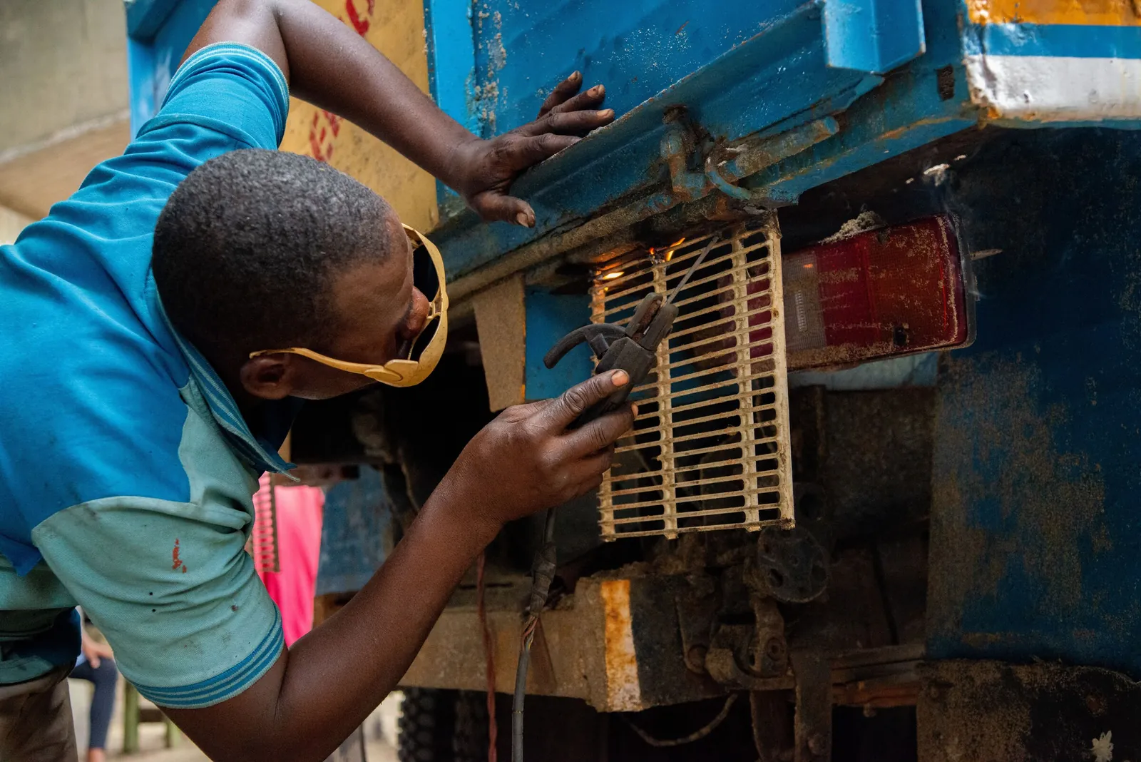 A mechanic in welding goggles working on the front of a blue lorry in Lagos