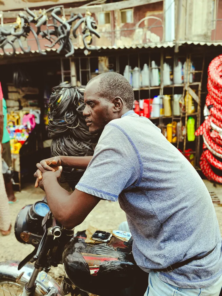 An okada rider in a blue shirt waiting on his motorcycle in a Lagos market