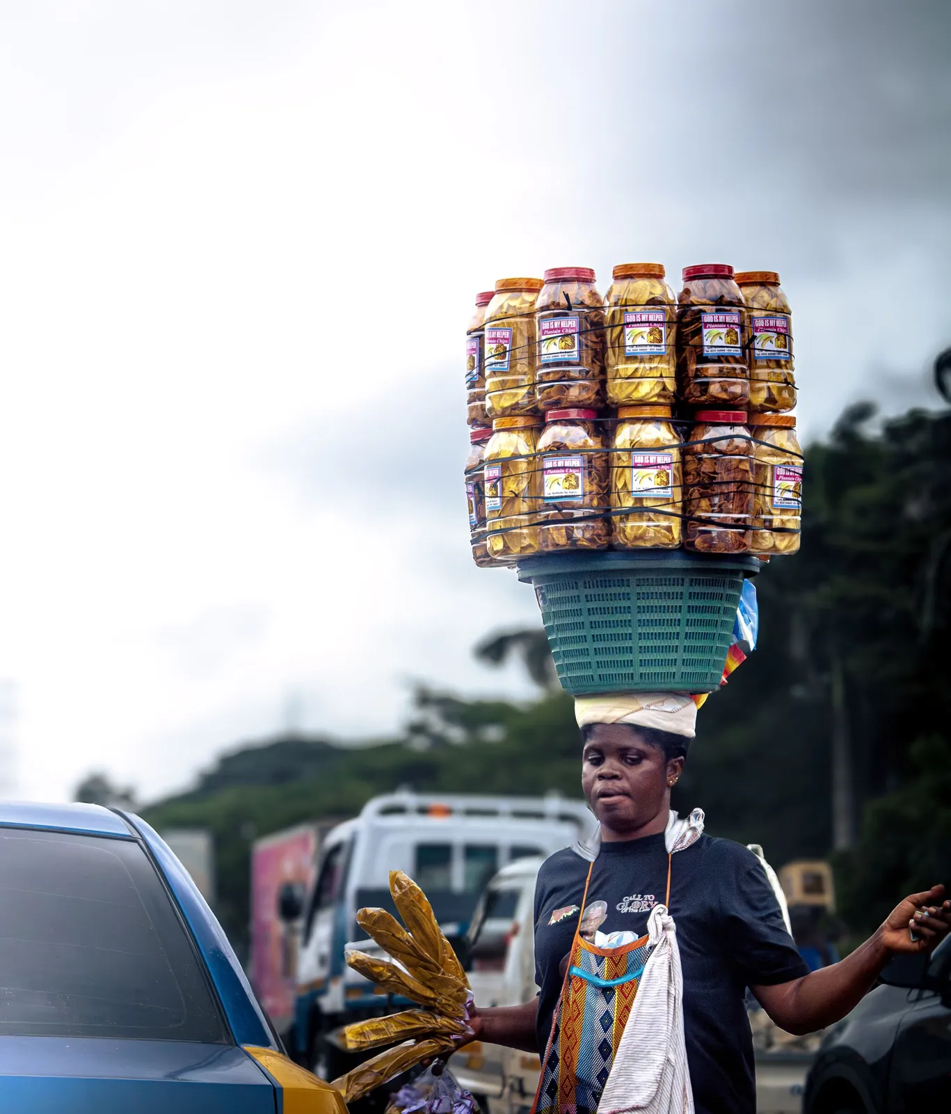 A woman in Accra carrying a tall stack of snack jars balanced on her head