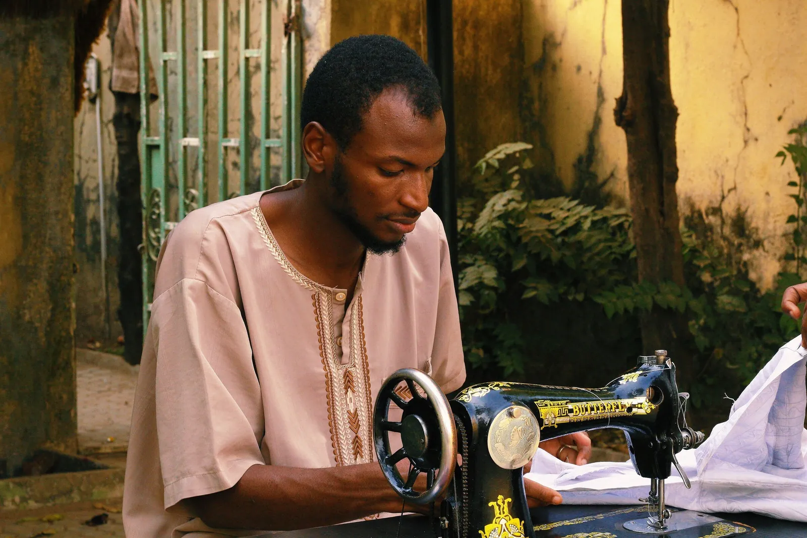 A tailor in a white kaftan sewing at a Butterfly machine outdoors