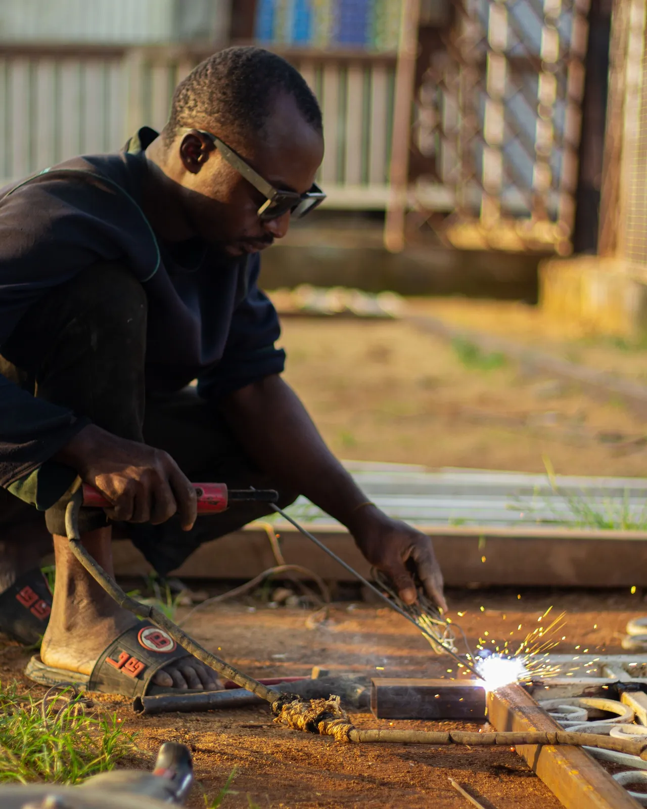 A welder in sunglasses working on a metal gate outdoors, sparks flying